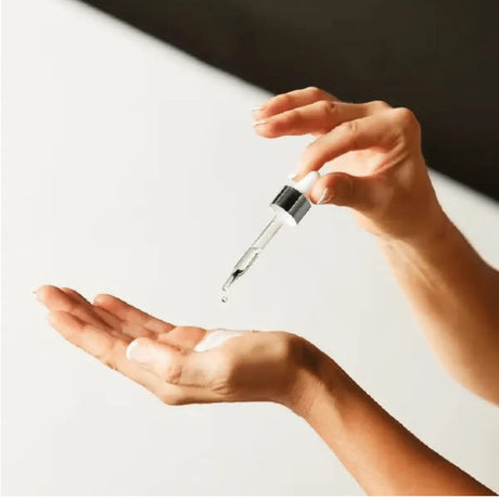 Produkten visas i bruk, med pipett, på ljus bakgrund – droppar som blandas med din dagliga fuktkräm för en solkysst look i ansikte och kropp.