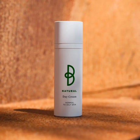 Vit tub med svart text, stående på mörk bakgrund – en dagkräm som ger lyster och balanserar huden.