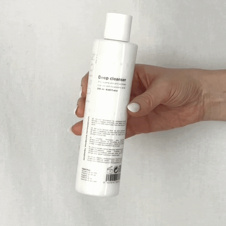 Vit flaska med svart text, visad i animerad rörelse mot ljus bakgrund – en rengöringsprodukt som återfuktar och rengör huden.