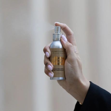 Silverfärgad sprayflaska med brun etikett, på ljus bakgrund – en mist som innehåller niacinamid och betaglukan för extra hudvårdsfördelar.