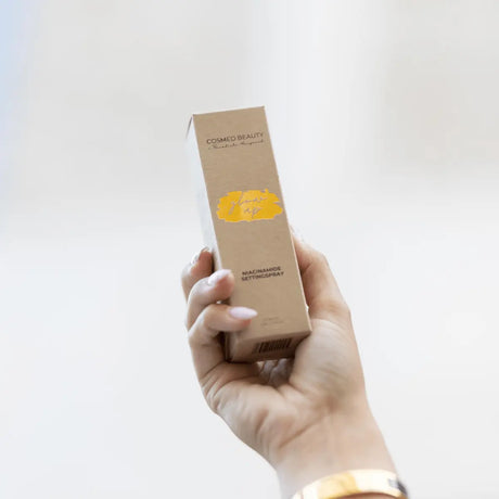 Brun pappkartong stående på ljus bakgrund – en setting spray som ger en naturlig lyster och håller sminket på plats hela dagen.