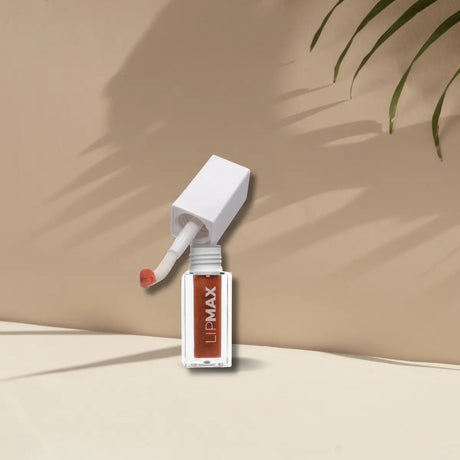 En brun läppglans med elegant, glansig förpackning syns på bilden. Produkten är genomskinlig nog att visa den krämiga konsistensen och ger intrycket av en fyllig, vårdande formula. Förpackningen är utformad för enkel applicering och har en modern, minimalistisk design som tilltalar en bred målgrupp. Produkten är vegansk och Cruelty-free och är framtagen för att ge läpparna en maxad fyllighet och glans.