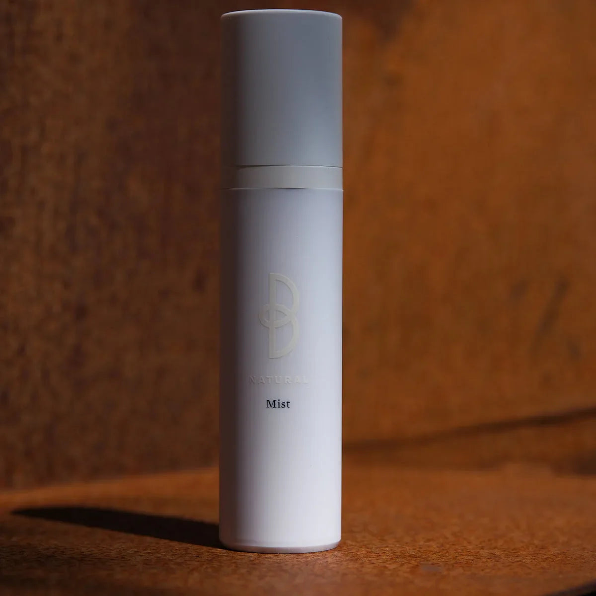 Vit sprayflaska med svart text, stående på mörk bakgrund – en uppfriskande ansiktsmist för daglig användning.