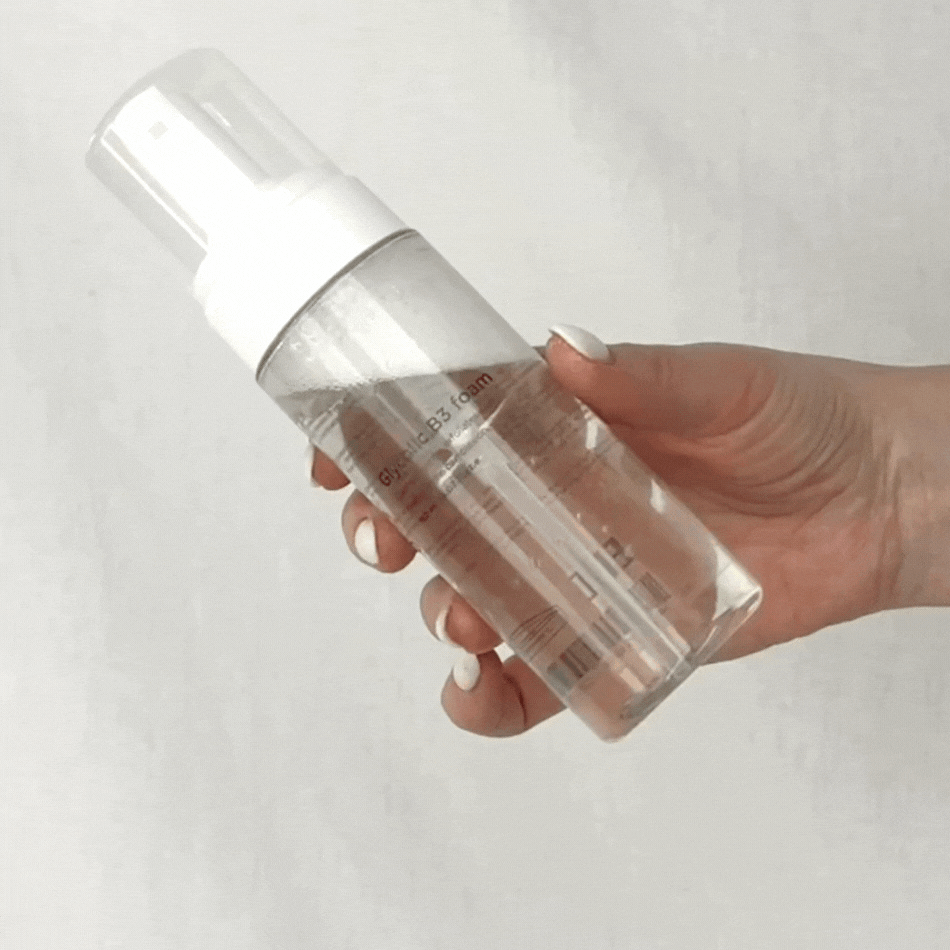 Vit flaska med svart text, visad i animerad rörelse mot ljus bakgrund – ett exfolierande rengöringsskum för alla hudtyper.