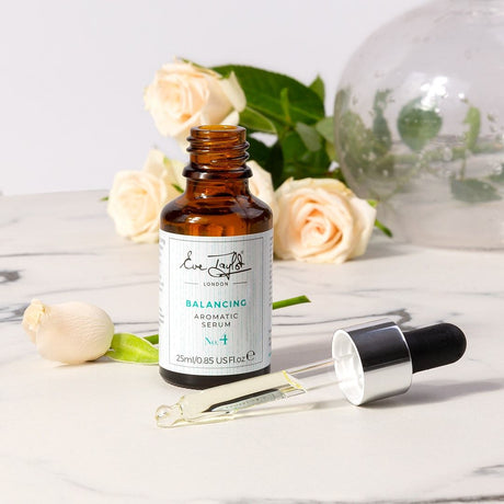 Balancing Aromatic Serum No.4 för normal hud presenteras i en stilren glasflaska med svart pump och silverkork. Flaskans etikett är enkel och elegant med svart text på vit bakgrund, vilket ger ett fräscht och lyxigt intryck. Produkten är avsedd att ge näring och balans till huden.