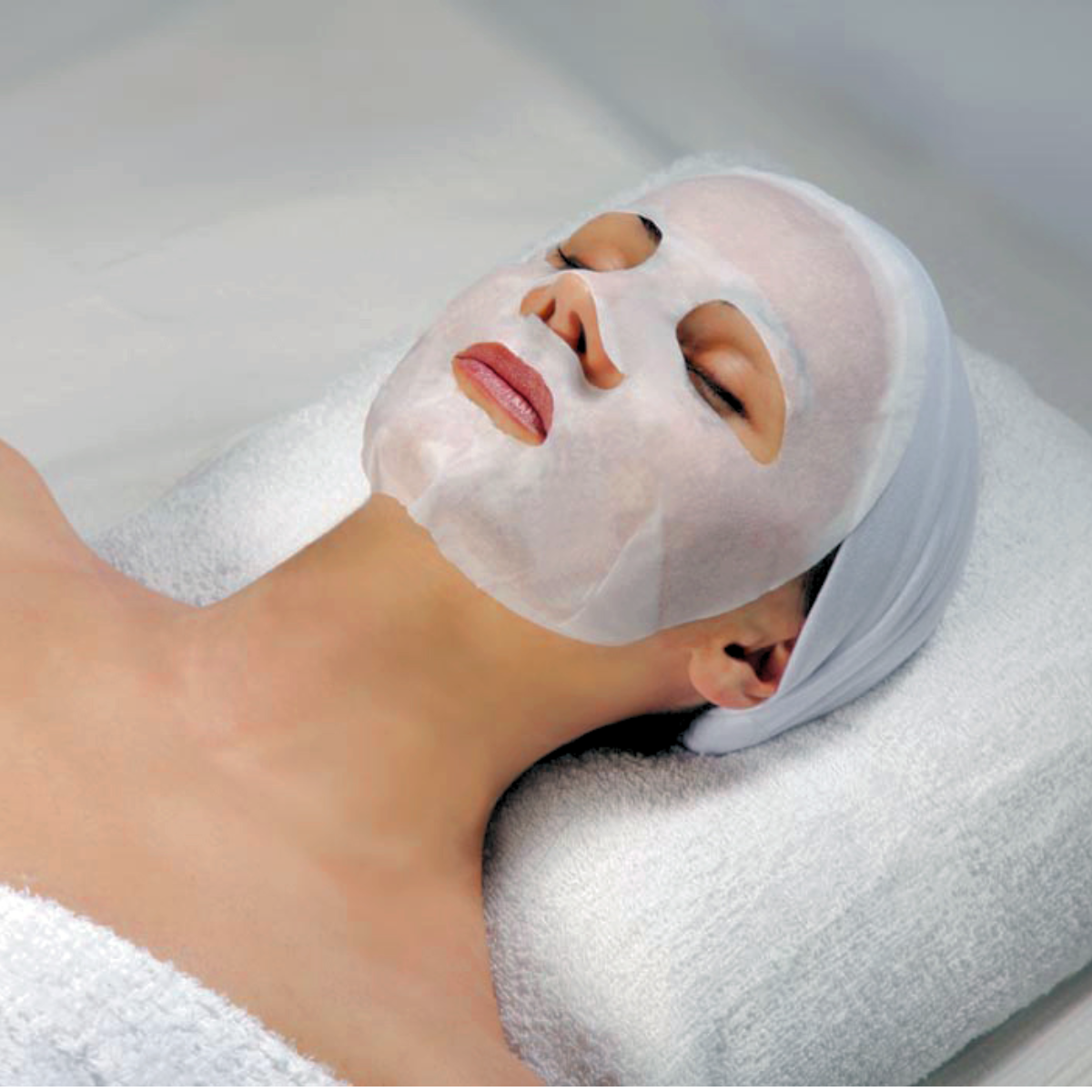 Vit mask på kvinna, liggande på ljus bakgrund – en ansiktsmask som kan användas med serum eller kaviarvätska.