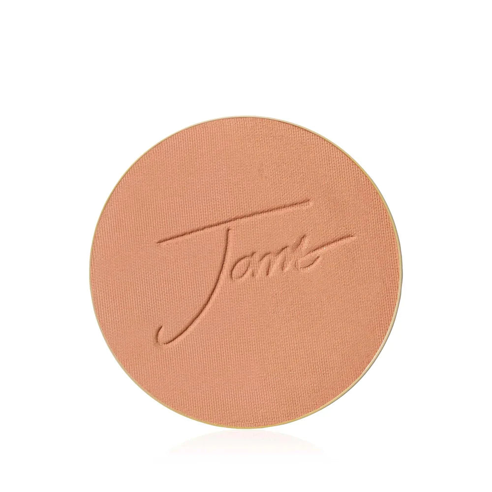 Ett runt bronzing-puder. Pudret har en varm, gyllene ton. Bilden har bra kontrast och visar tydligt pudrets struktur.